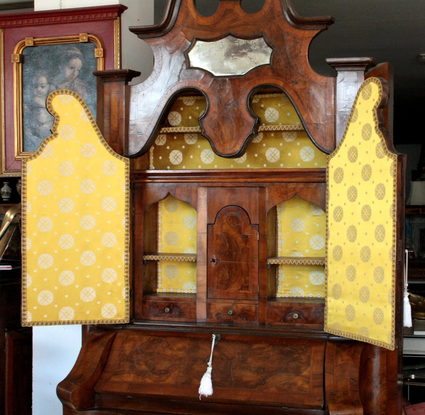 Trumeau lombardo originale in noce con linea trapezoidale elegante e corpo mosso presenta scaffali aperti rivestiti in tessuto giallo